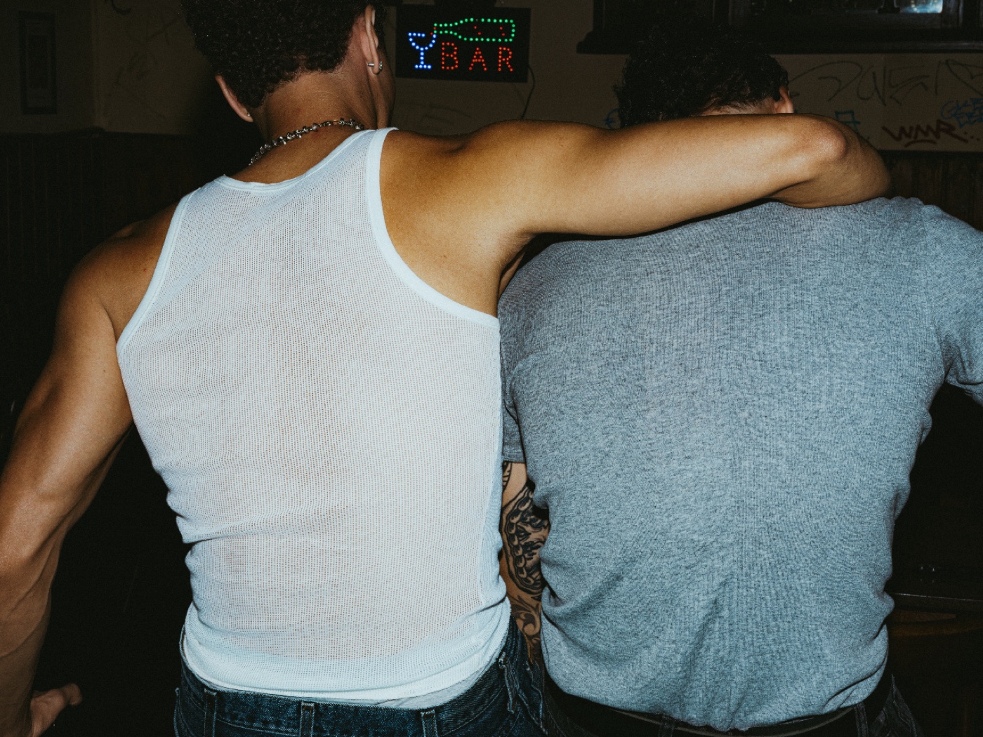 Two friends arm in arm at a bar